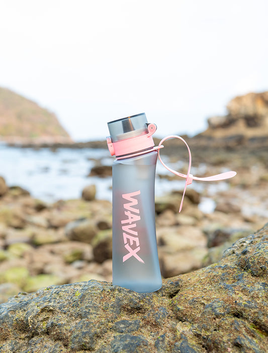 A 600ml pink water bottle with a strap rests on a rock, showcasing its stylish design and coffee taste bud feature.